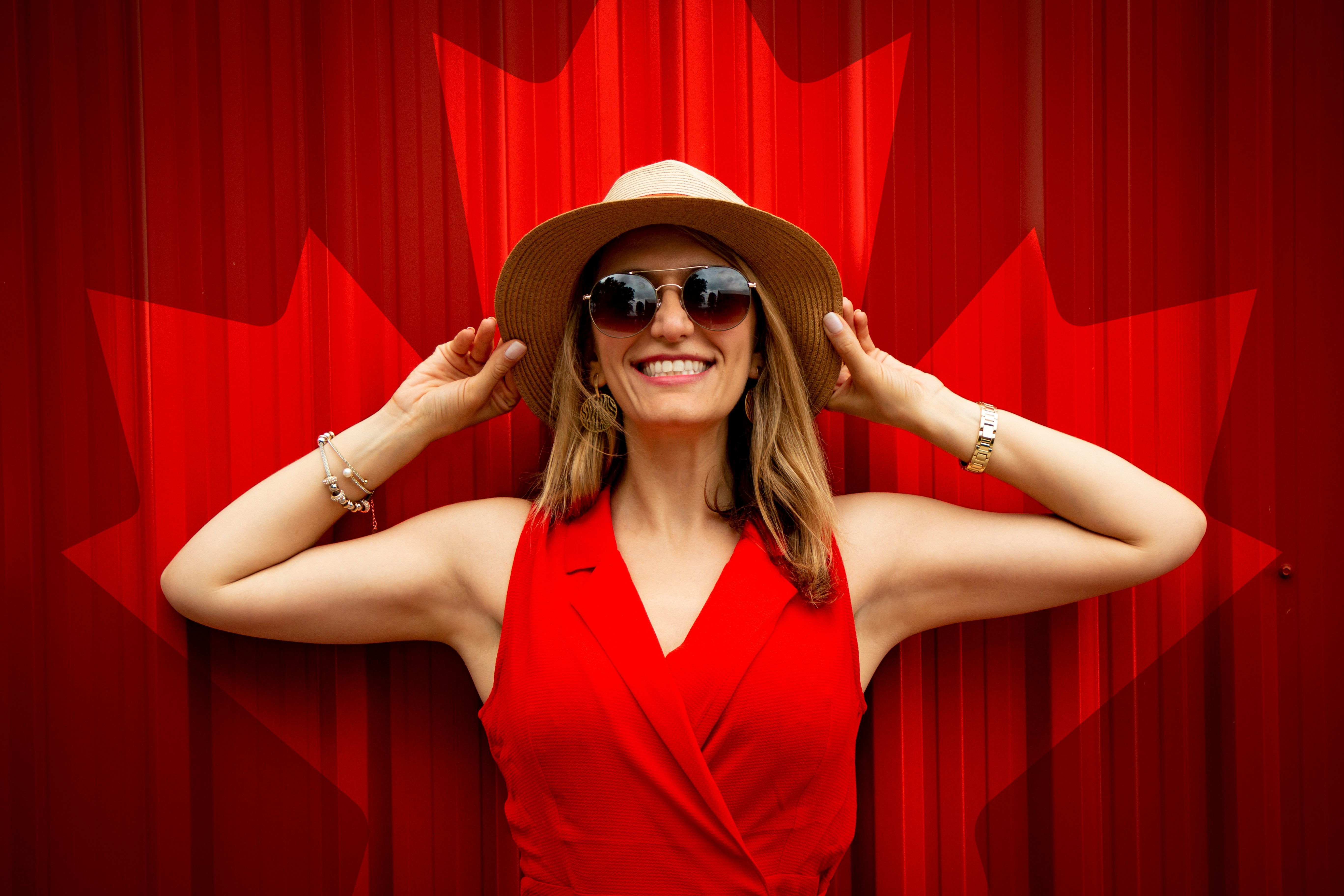 woman in red sleeveless top holding her hat while smiling
